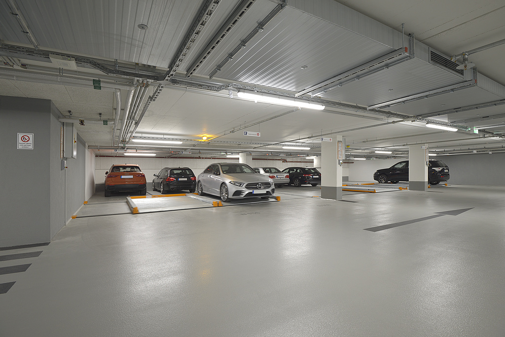 Cars are parked in an underground car park, a parking pallet with a vehicle is being moved in front of it