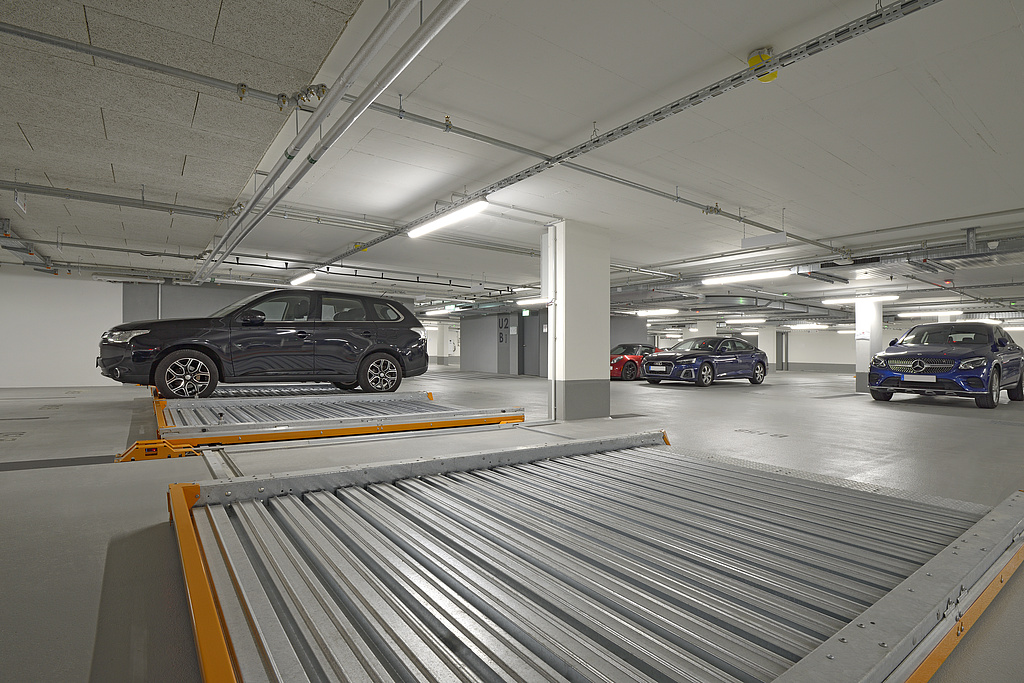 Parking pallets with a vehicle can be seen in close-up, an underground car park with parked cars in the background