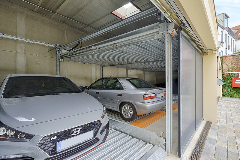 Two cars can be seen in a parking system through an open sliding gate