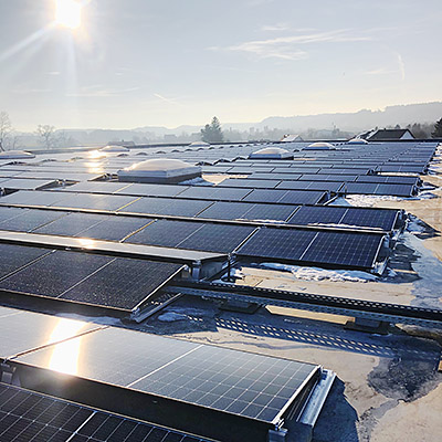 Sonne am Himmel, Sonnenstrahlen spiegeln sich in den Photovoltaik-Anlagen auf einem Firmendach