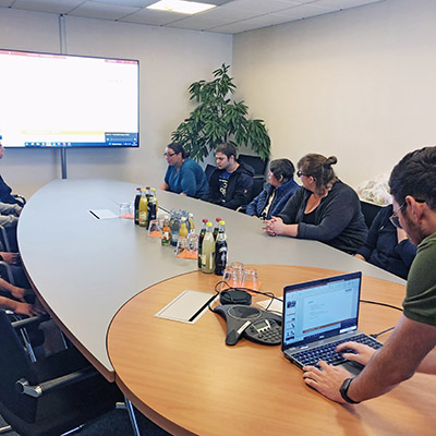 Mehrere Personen sitzen in einem Konferenzraum vor einem Präsentationsmonitor