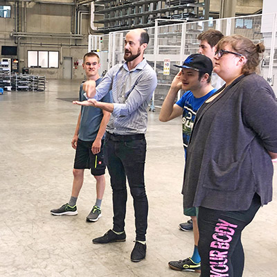 In a production hall, several people are standing around a man who is explaining something