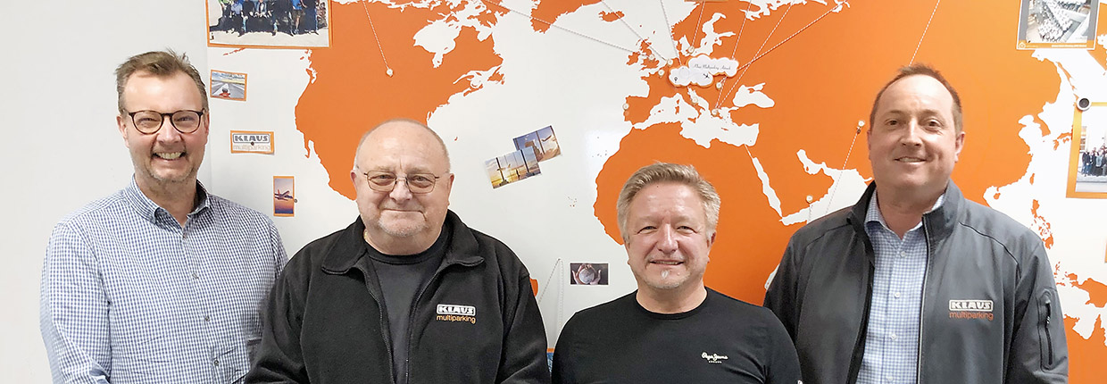 Four men looking forward, in the background a world map in orange