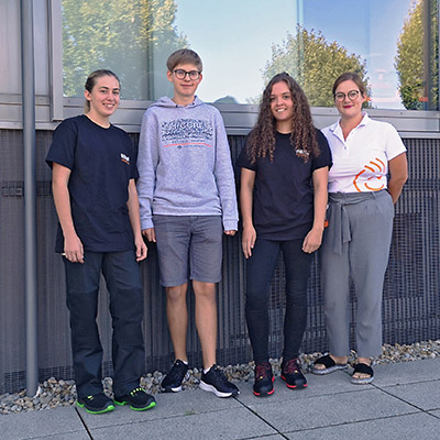 Four young persons are standing in front of a company building